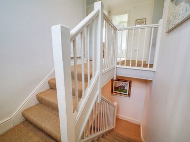 A staircase with beige carpet and white railings with a framed picture on the wall at Worthy House in Daymer Bay