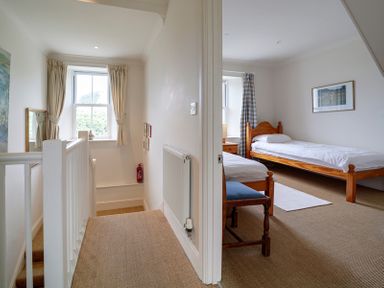 A hallway with a window and a chair next to two beds in a bedroom at Worthy House in Daymer Bay