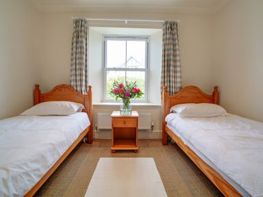 A bedroom with two single wooden beds and a nightstand with flowers between at Worthy House in Daymer Bay