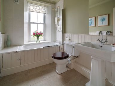 A bathroom with a bathtub flowers in a vase toilet and sink at Worthy House Daymer Bay