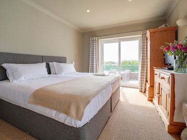 A bedroom with a double bed a wooden dresser a wooden wardrobe and sliding glass doors at Worthy House in Daymer Bay