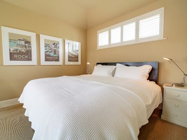 A bedroom with a double bed white bedding bedside tables lamps and framed pictures on the wall at Worthy House in Daymer Bay