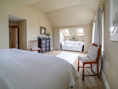 A bedroom with a bed wooden chairs a cabinet a white sofa under skylights and a rug on the floor at Worthy House in Daymer Bay