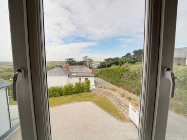 A view of a garden with grass gravel driveway and bushes seen through a closed window at Worthy House in Daymer Bay