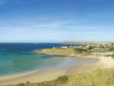 A beach with sandy shore and blue ocean with houses and cars near the coast at Worthy House in Daymer Bay
