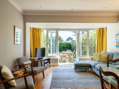 A living room with gray chairs blue sofa yellow curtains and a view to a garden at Lowenna Manor 4 in Rock