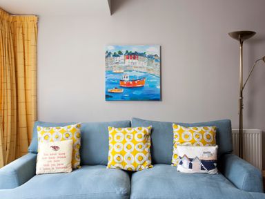 A blue sofa with yellow patterned and printed cushions against a white wall with a painting of boats above at Lowenna Manor 4 in Rock