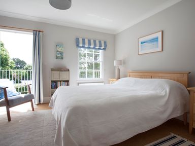 A bedroom with a double bed a chair a bookshelf and a window with blue and white curtains at Lowenna Manor 4 in Rock