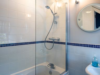 A bathroom with a bathtub shower combination white tiled walls and a round mirror above a sink at Lowenna Manor 4 in Rock