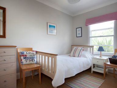 A bedroom with a single bed white bedding a wooden chair with a cushion a white nightstand with blue lamp and a window at Lowenna Manor 4 in Rock