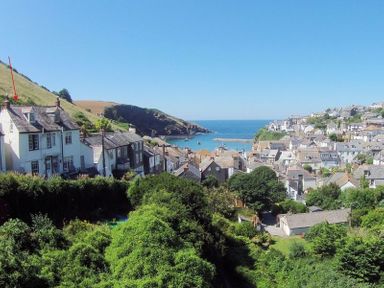 A coastal village with houses on a hillside overlooking the ocean and boats in the water at April Cottage in Port Isaac