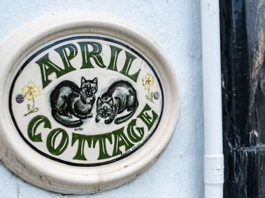 A ceramic sign with two cats and green text reading April Cottage on a white wall at April Cottage in Port Isaac