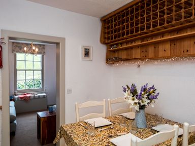 A dining area with a table set with plates and glasses and a flower vase at April Cottage in Port Isaac