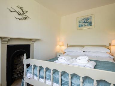 A bedroom with a double bed with folded towels bedside tables lamps a fireplace and wall decorations at April Cottage in Port Isaac