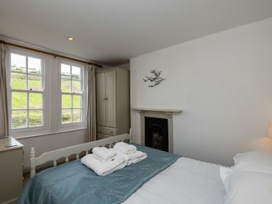 A bedroom with a bed and folded towels near two windows and a wardrobe at April Cottage in Port Isaac