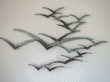 Metal wall art of birds flying mounted on a white textured wall at April Cottage in Port Isaac