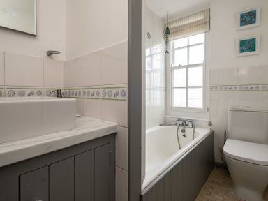 A bathroom with a bathtub under a window a toilet and a sink at April Cottage in Port Isaac