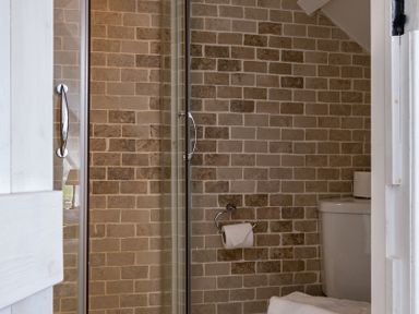 A bathroom with a glass shower door a toilet and a wall-mounted toilet paper holder at April Cottage in Port Isaac