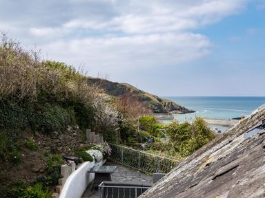 An outdoor patio area with a table and chairs overlooking a hillside and a coastal view at April Cottage in Port Isaac