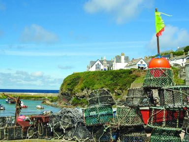 A harbor with lobster traps stacked in the foreground and houses on a cliff overlooking the sea at April Cottage in Port Isaac
