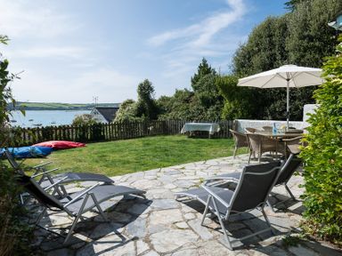 A garden with sun loungers a table with chairs and an umbrella by a fence overlooking water at Carn Du 1 in Rock
