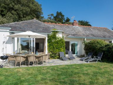 A garden patio with a dining table and umbrella and lounge chairs in front of a white house at Carn Du 1 in Rock