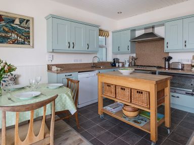 A kitchen with a wooden island three wicker baskets a dining table with plates and glasses and light blue cabinets at Carn Du 1 in Rock