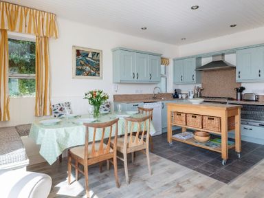 A kitchen with blue cabinets a wooden island table and a dining table with chairs and green tablecloth at Carn Du 1 in Rock