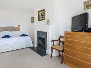 A bedroom with a bed fireplace wooden chair dresser with a television on top at Carn Du 1 Rock