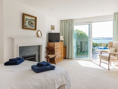 A bedroom with a bed folded towels fireplace wooden chest of drawers armchair and sliding glass door at Carn Du 1 in Rock