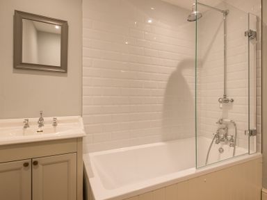 A bathroom with a bathtub shower combination and a sink with a mirror at Carn Du 1 in Rock