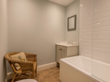A bathroom with a wicker chair with cushions a sink with a mirror and a bathtub at Carn Du 1 in Rock