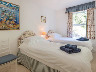 A bedroom with two single beds a window with floral curtains and a chair at Carn Du 1 in Rock