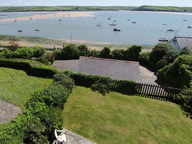 A garden with hedges and a gate overlooking a body of water with boats and a beach at Carn Du 1 in Rock
