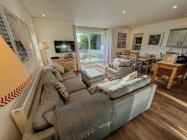 A living room with gray sofas a television on a wooden cabinet and a dining table with chairs at Carn Du 1 in Rock