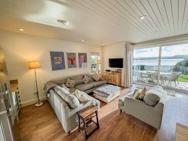 A living room with sofas a wooden cabinet and a large sliding door opening to an outdoor dining area at Carn Du 1 in Rock