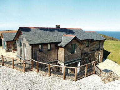 A wooden house with a fenced gravel area and a stone patio near the coast at Ossco in Polzeath