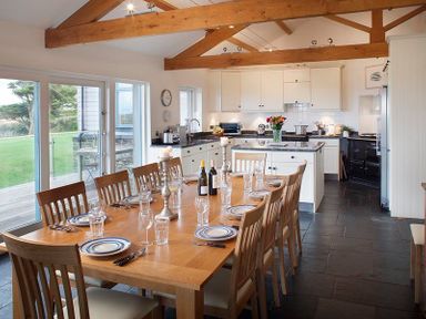 A kitchen and dining area with a wooden dining table set for eight and white cabinets at Ossco in Polzeath
