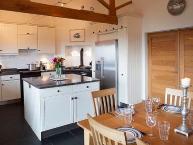 A kitchen with a dining table set with plates glasses and cutlery at Ossco in Polzeath