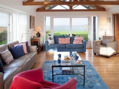 A living room with sofas and a glass coffee table overlooking the sea at Ossco in Polzeath
