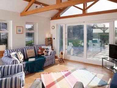 A living room with striped sofas a wooden floor and large glass doors at Ossco Polzeath