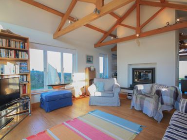A living room with wooden ceiling beams a fireplace a bookshelf a television and seating at Ossco Polzeath