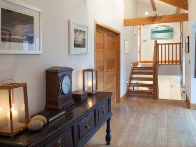 A hallway with a wooden table holding a clock candles and stones beside wooden stairs at Ossco Polzeath
