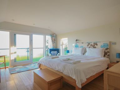 A bedroom with a double bed a blue armchair and sliding glass doors at Ossco in Polzeath