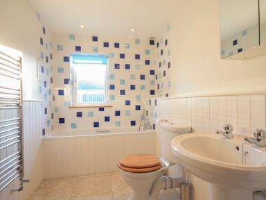 A bathroom with a bathtub tiled with blue squares a toilet with a wooden seat a sink and a heated towel rail at Ossco in Polzeath