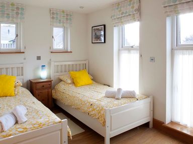 A bedroom with two single beds yellow and white bedding and a wooden nightstand with a lamp at Ossco in Polzeath