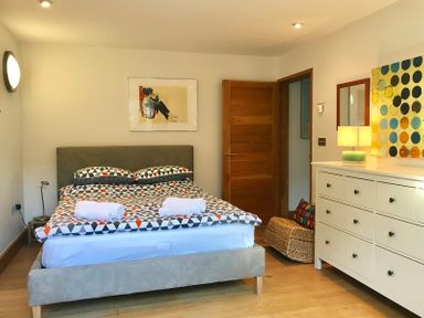 A bedroom with a bed a dresser a lamp and two paintings at Ossco in Polzeath