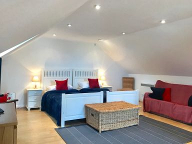 A bedroom with two single beds with red pillows a wicker chest a red sofa and wooden furniture at Ossco in Polzeath