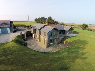 A two-story house with stone lower walls and wooden upper walls surrounded by a grass lawn at Ossco in Polzeath