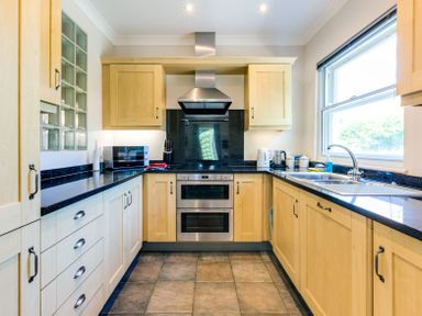 A kitchen with wooden cabinets black countertops a stove microwave kettle and a window at Lowenna Manor 10 in Rock